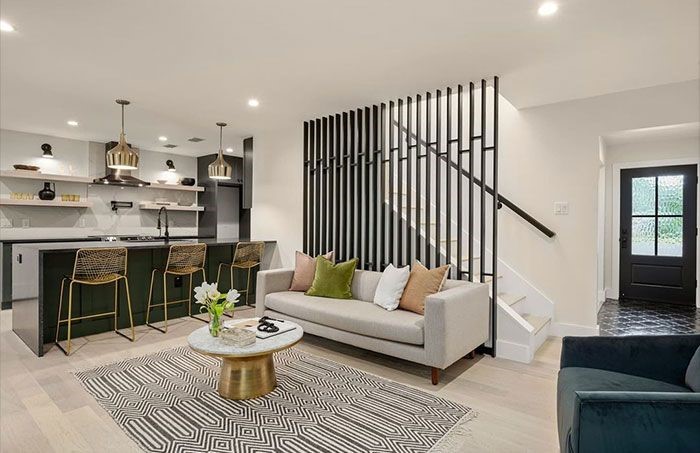 A modern open-concept living area features light floors, a gray sofa with colorful cushions, a gold coffee table, and a black kitchen island.