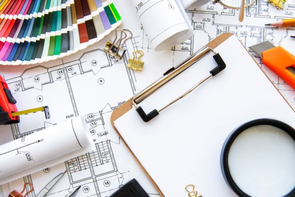 A desk with design tools—color swatch, blueprints, clipboard, magnifying glass, and binder clips—suggests an architect's workspace.